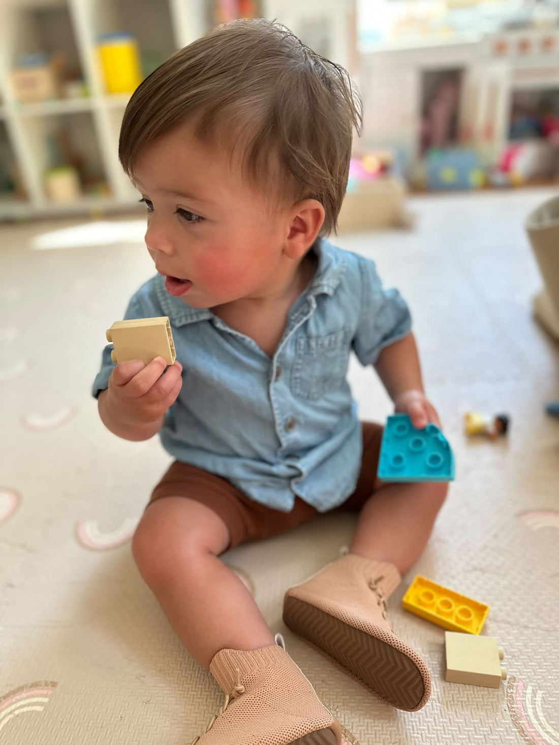 Toddler playing with wooden blocks in neutral barefoot toddler boots designed for healthy foot development