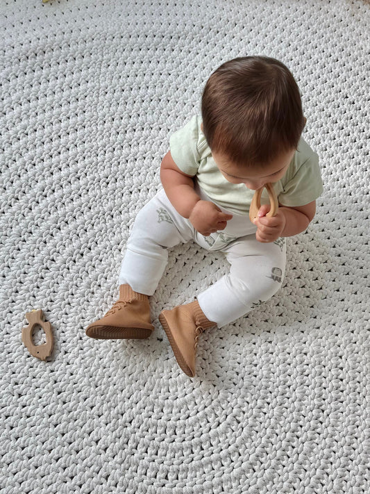 1-year-old baby playing with a wooden toy while wearing HARTS Bootees barefoot boots that stay on and support natural movement.