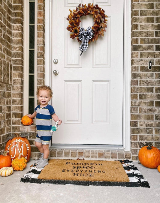 Toddler sitting on a front porch with pumpkins, wearing HARTS Bootees barefoot boots for fall.