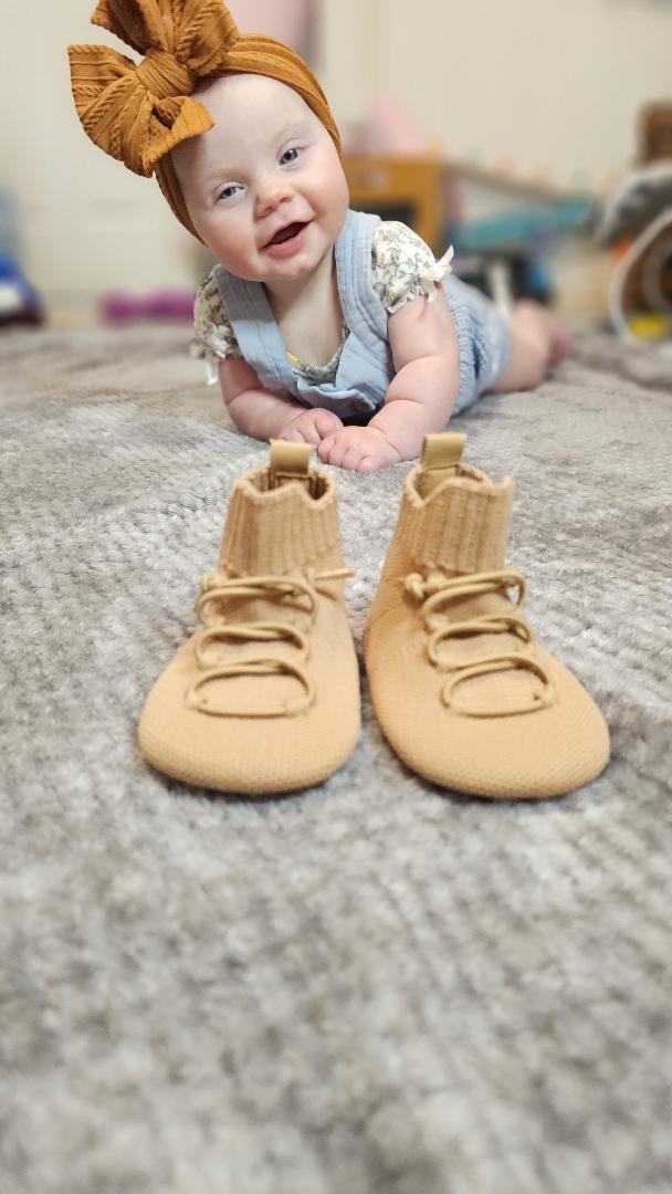 Baby smiling on the floor indoors wearing HARTS soft-sole shoes during everyday play