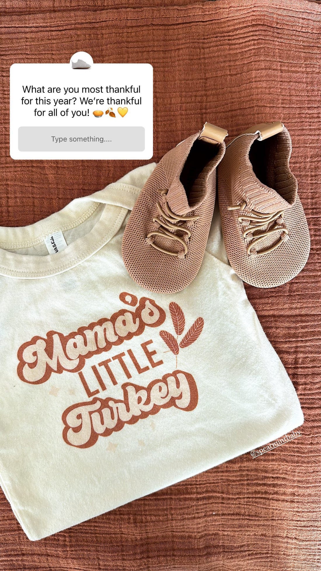 Flat lay of tan knit HARTS Bootees barefoot boots beside a cream “Mama’s Little Turkey” toddler tee on a rust-colored fabric — cozy Thanksgiving outfit for babies and toddlers.